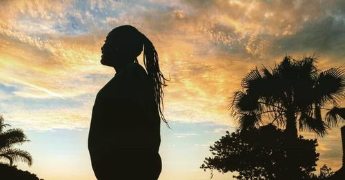 Silhouette person standing by palm tree against sky during sunset