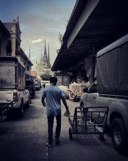 Rear view of man walking on street amidst buildings