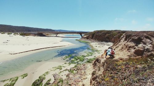 Rear view of woman photographing on rock formation at pescadero state beach