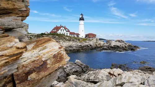 Lighthouse and houses by sea against blue sky