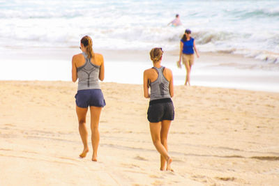Rear view full length of female friends walking at beach