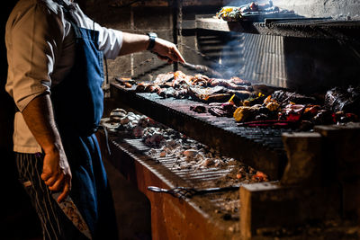 Midsection of chef preparing food on barbecue grill