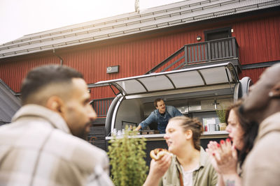 Group of friends talking with each other while male owner working in background at food truck
