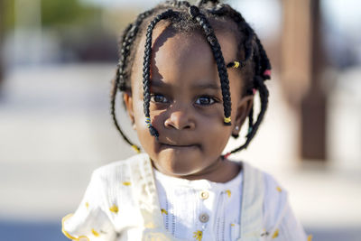 African american little girl with braids in stylish clothes standing on street against building in sunny day