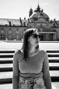 Young woman looking away while standing against built structure