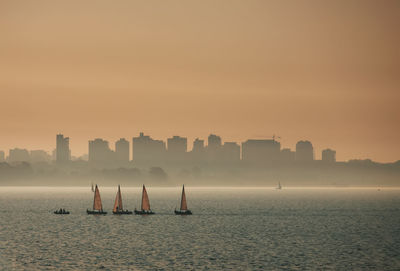 Silhouette buildings by sea against sky during sunset