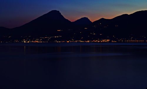 Illuminated city by silhouette mountain against sky at night