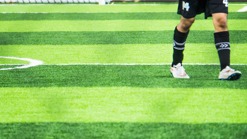 Low section of man playing soccer on field seen through chainlink fence