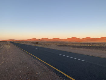 Road leading towards mountains against clear sky