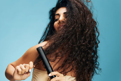 Close-up of woman using straightener against wall