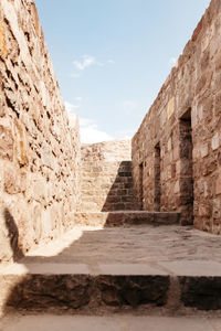 Empty footpath leading towards steps amidst weathered wall