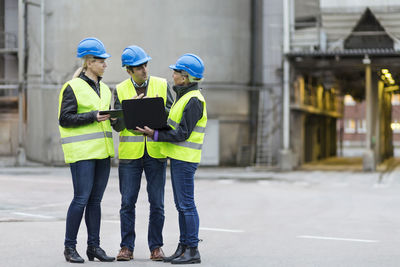 Full length of manual workers using technologies at factory