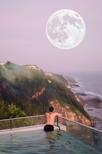 Rear view of man swimming in infinity pool during night