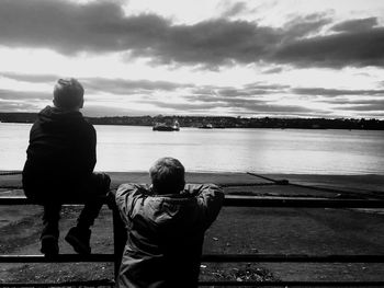 Rear view of boys looking at sea against cloudy sky