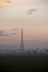 Electricity pylon on field against sky at sunset