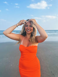 Portrait of young woman standing at beach against sky