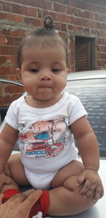 Baby girl sitting on car against brick wall