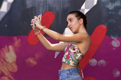 Young woman with arms raised standing against wall