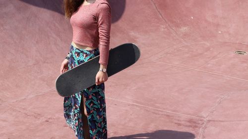 Midsection of fashionable young woman holding skateboard while standing on sports ramp