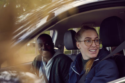 Young woman and man looking away while sitting in car
