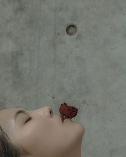 Close-up of young woman with rose shape ring in mouth against wall