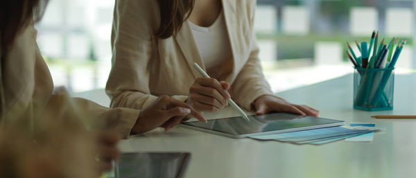 Midsection of colleagues discussing over digital tablet on desk