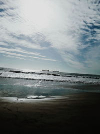 View of calm beach against cloudy sky