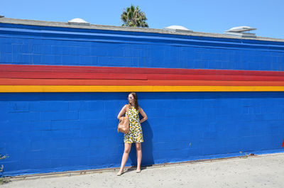 Woman standing against blue wall during sunny day