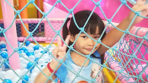 Portrait of cute girl gesturing peace sign by fence