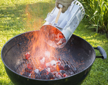 Close-up of cropped hand putting burning coals in barbecue grill