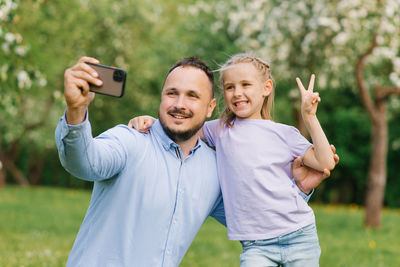 Dad and his six-year-old daughter take selfies on the phone, smiling and having fun on camera