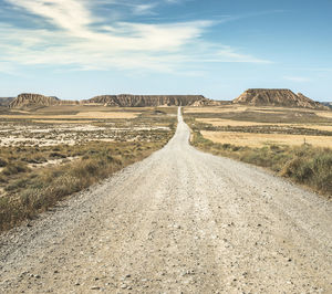 Dirt road leading towards mountains against sky