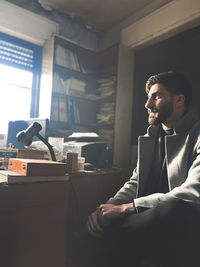 Side view of young man using mobile phone while sitting at home