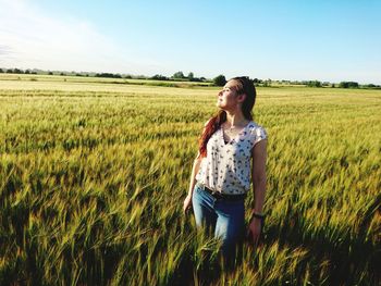 Young woman standing on field against sky