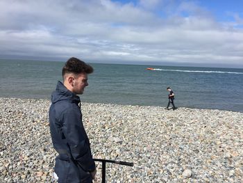 Side view of young man standing at beach against sky