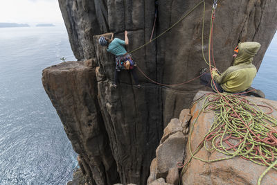 Adventurous couple climbs the exposed rock pilars of cape raoul, with the woman using two ropes as protection as she tries to find a way up, and the man belaying her in tasmania, australia.