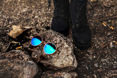 Low section of woman standing by sunglasses on rock