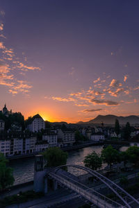 High angle view of buildings by river against sky during sunset