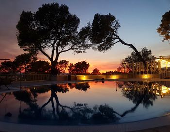 Silhouette trees by swimming pool against lake during sunset