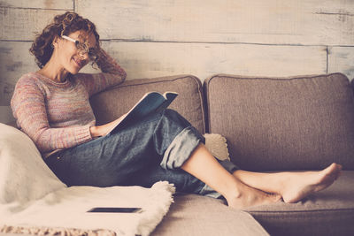 Young woman reading book while relaxing on sofa at home