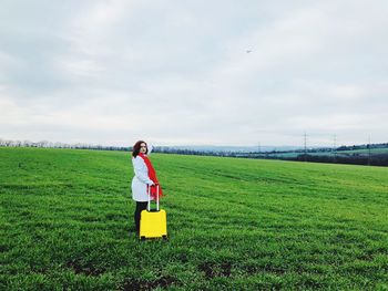 Woman holding luggage while standing on field