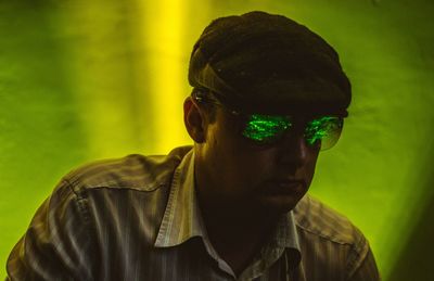 Close-up of mid adult man wearing sunglasses against green illuminated wall