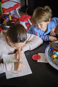 High angle view of boy looking at mother writing on paper