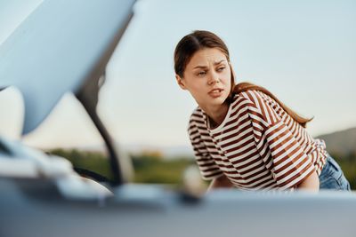 Portrait of smiling young woman sitting on car