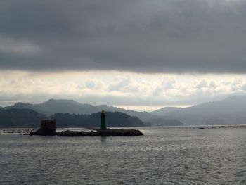 Mid distance view of lighthouse on groyne in sea against cloudy sky