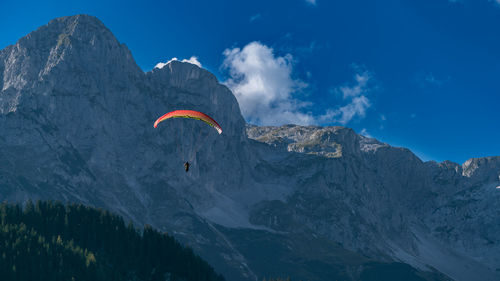 Low angle view of people flying over mountain against sky