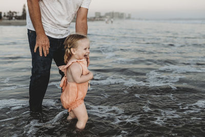 Toddler girl splashing in ocean with father at sunset