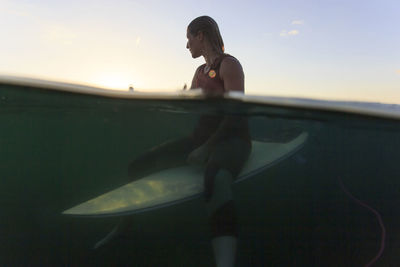 Woman sitting on surfboard in sea against sky