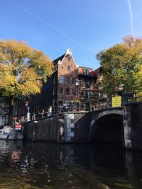 Arch bridge over river by buildings against sky