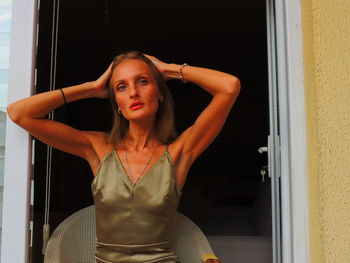 Portrait of young woman standing against window at home